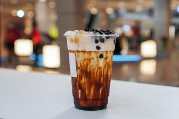 A plastic cup of fresh milk and brown sugar syrup, topped with boba or bubble tapioca pearl on white table.